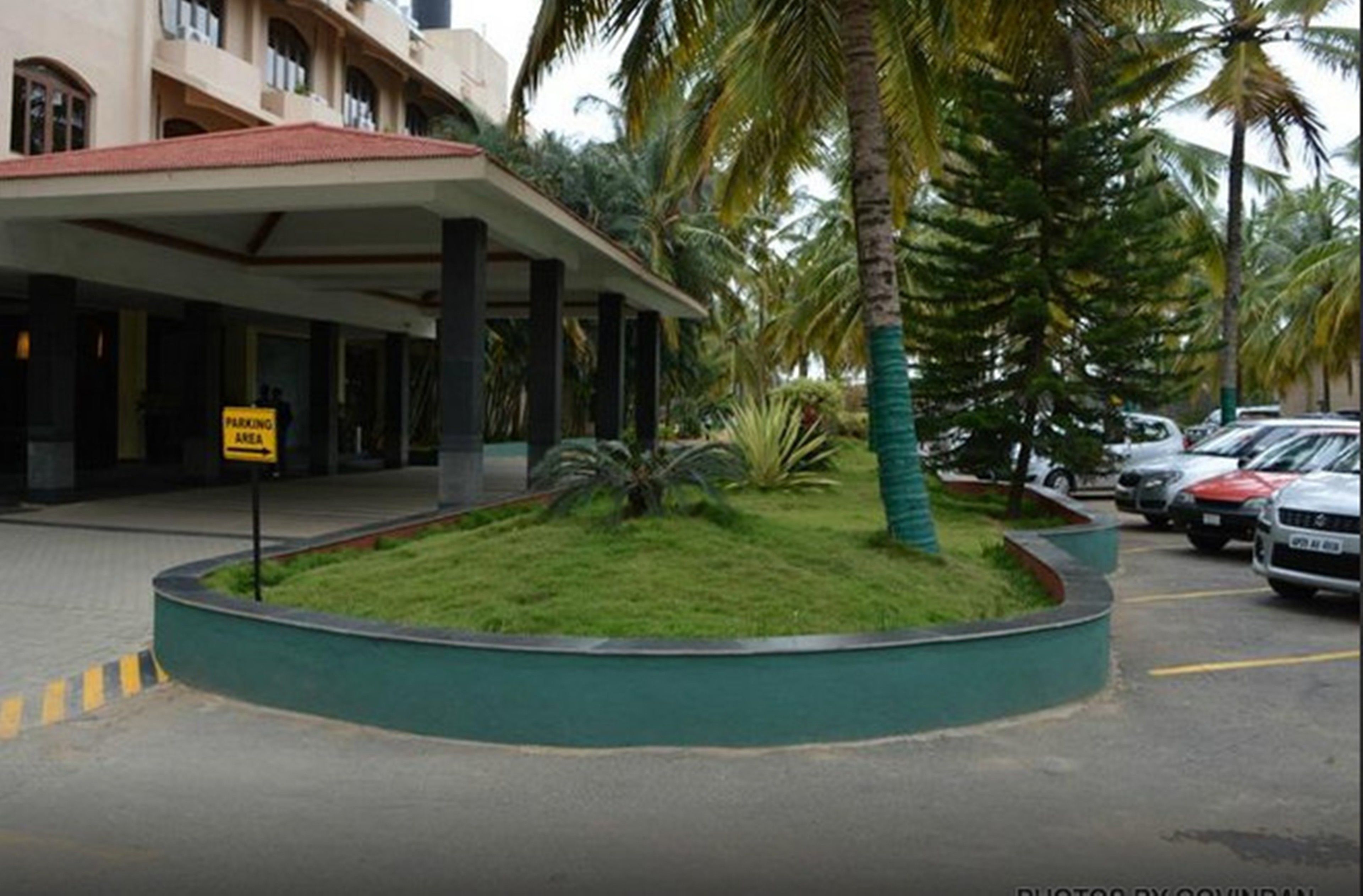 A hotel entrance with a covered walkway, palm trees, and a parking area sign.