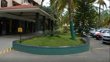 A hotel entrance with a covered walkway, palm trees, and a parking area sign.