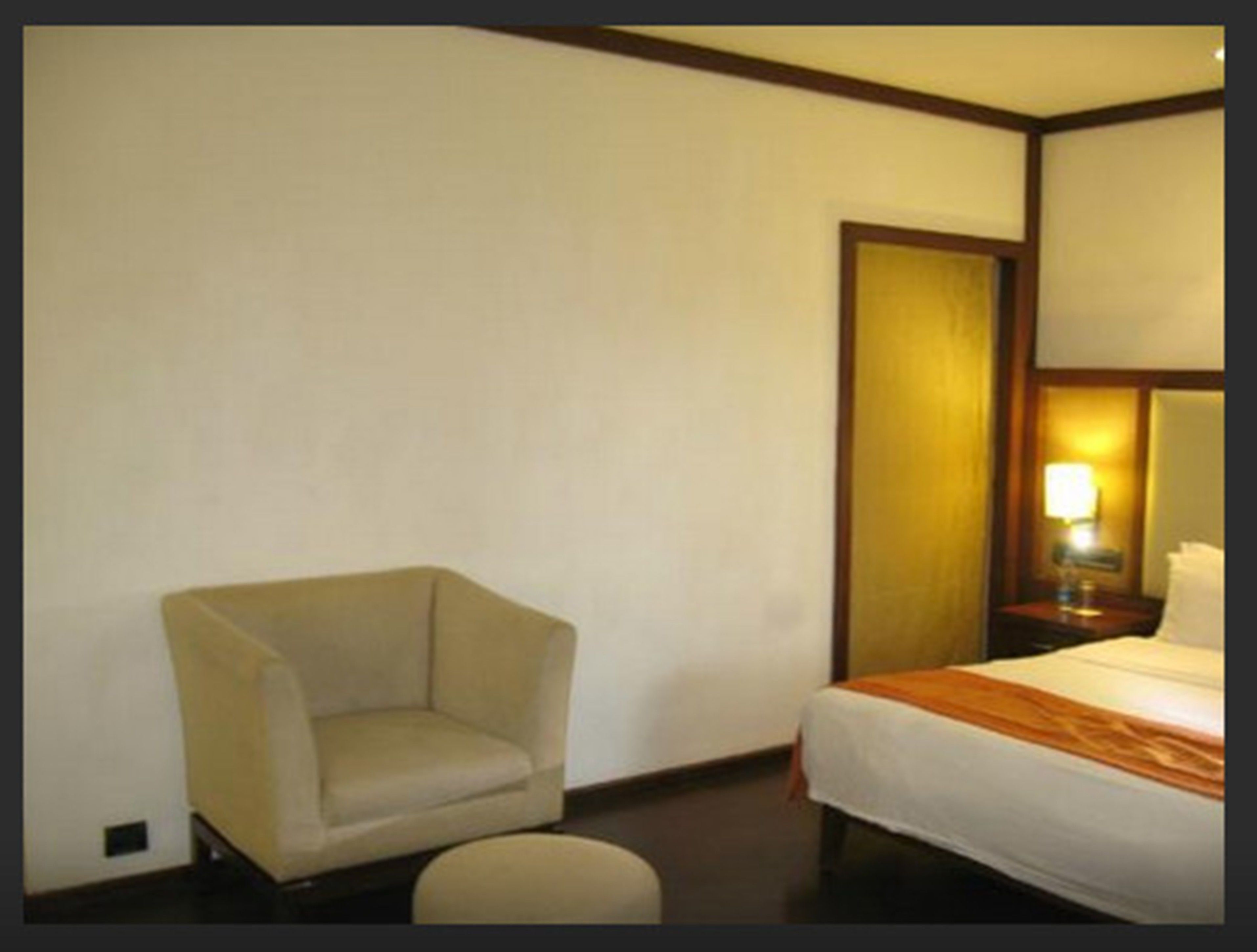 A hotel room with a single bed, a chair, and a nightstand with a lamp.