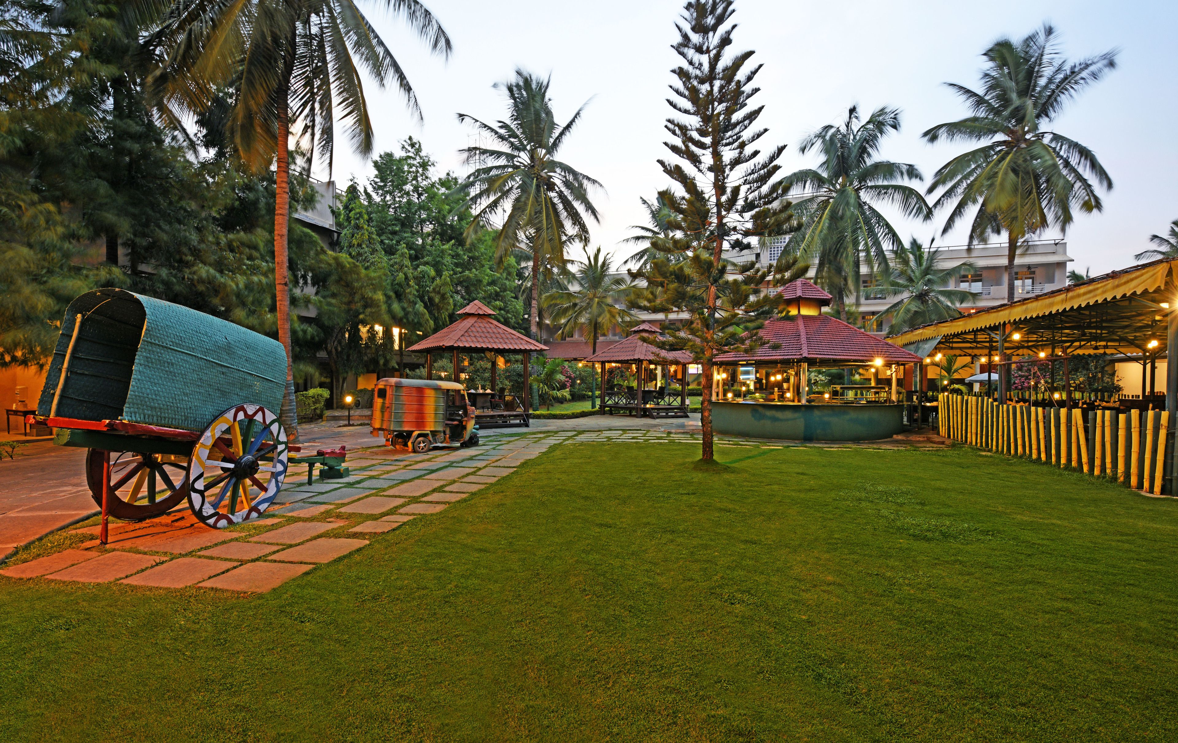 A well-maintained garden area with a traditional rickshaw, a gazebo, and a restaurant with outdoor seating.