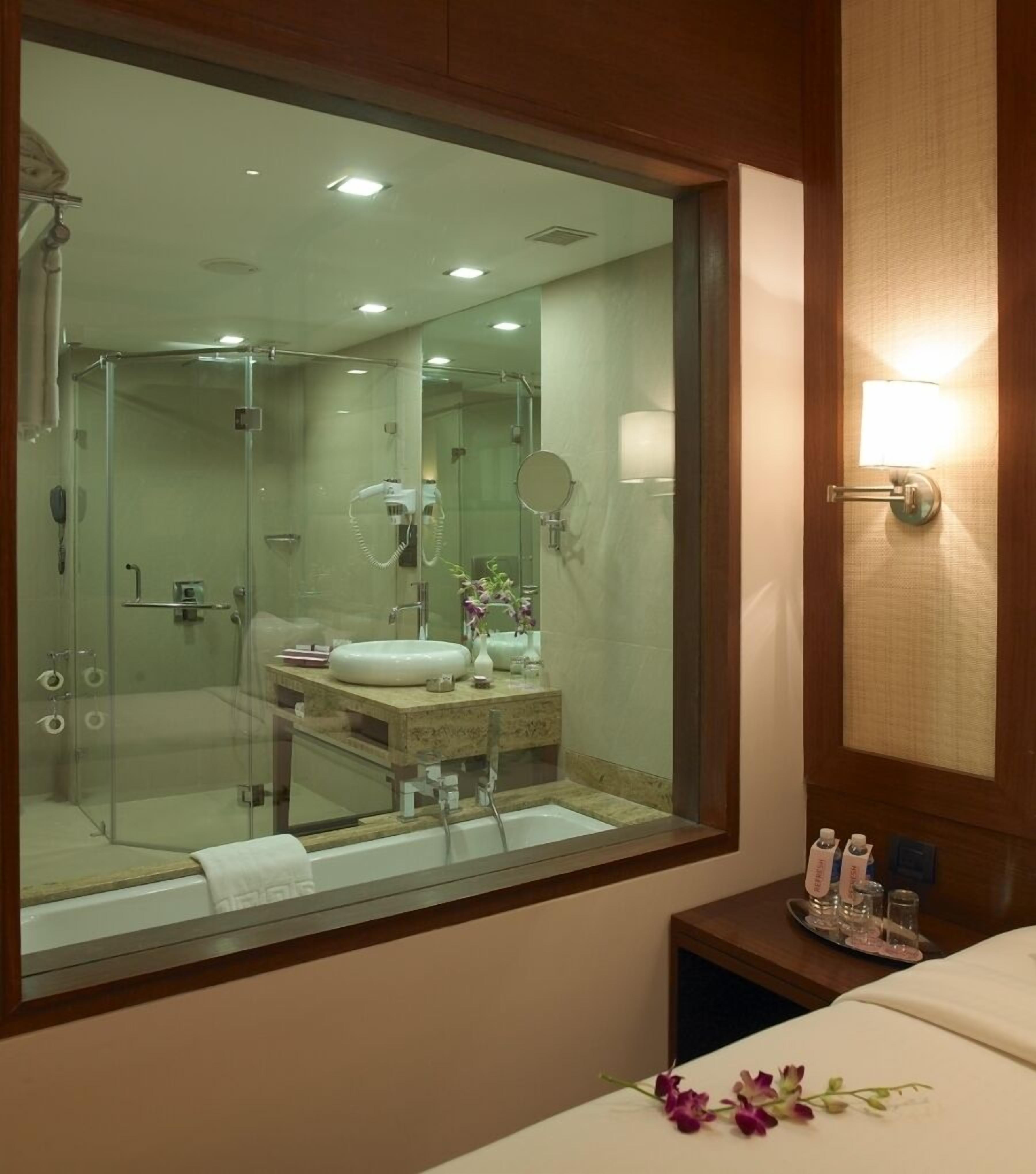 Baño de hotel con un espejo grande, un lavamanos, ducha y tocador con artículos de aseo.