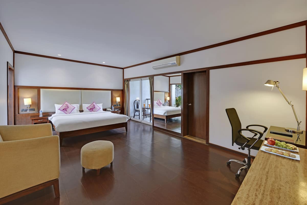 Ein Hotelzimmer mit einem großen Bett, einem Schreibtisch mit Lampe, einem Sessel und einem kleinen Tisch mit Snacks.