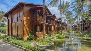 A wooden resort with multiple bungalow-style buildings, a central water feature, and lush tropical landscaping.