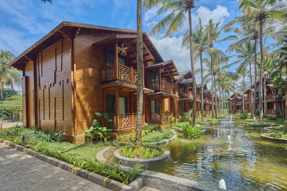 Ein Holz-Resort mit mehreren bungalowsartigen Gebäuden, einer zentralen Wassereinrichtung und üppiger tropischer Bepflanzung.