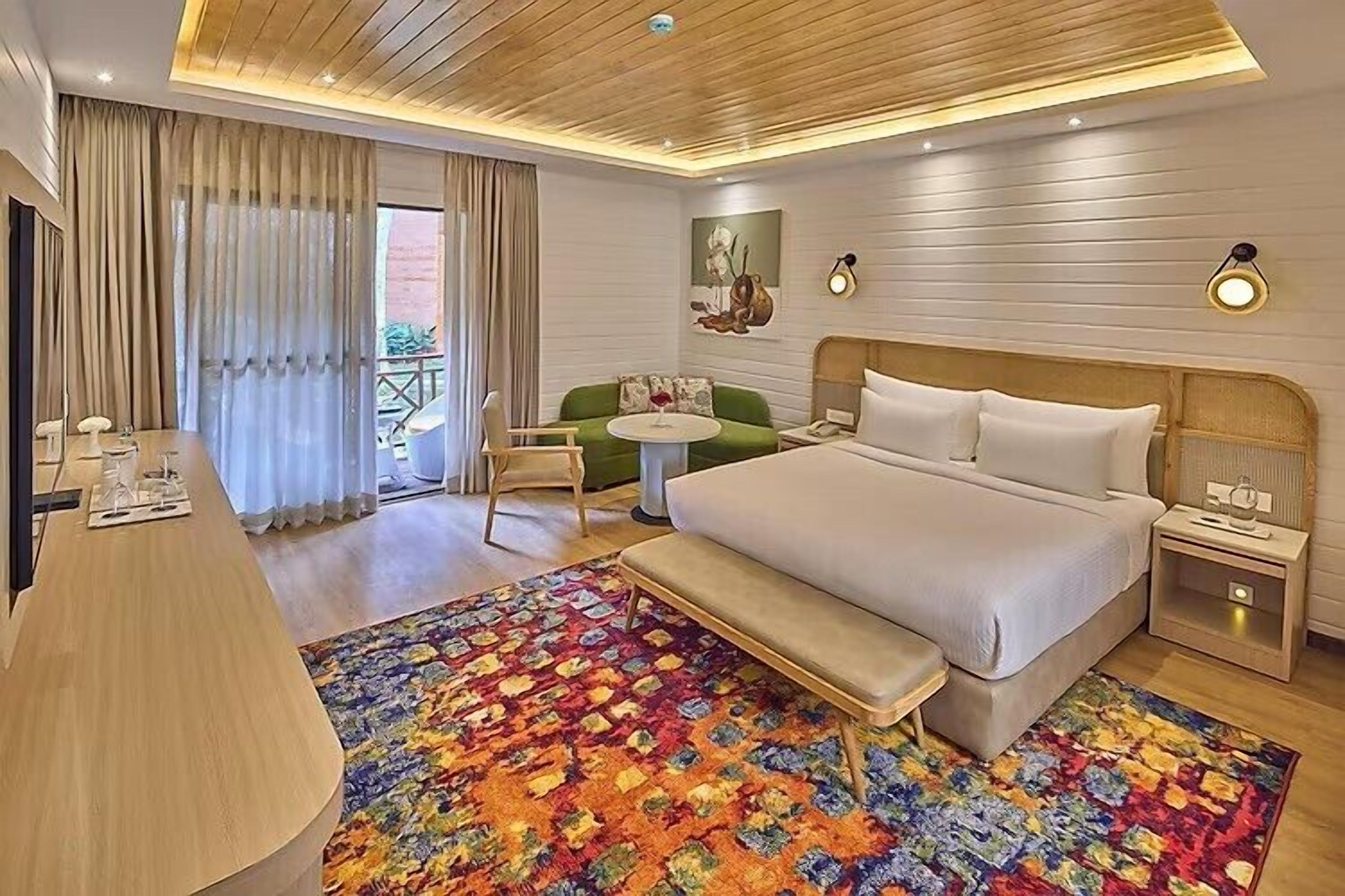 A hotel room with a large bed, a desk, a small round table, and a colorful rug.