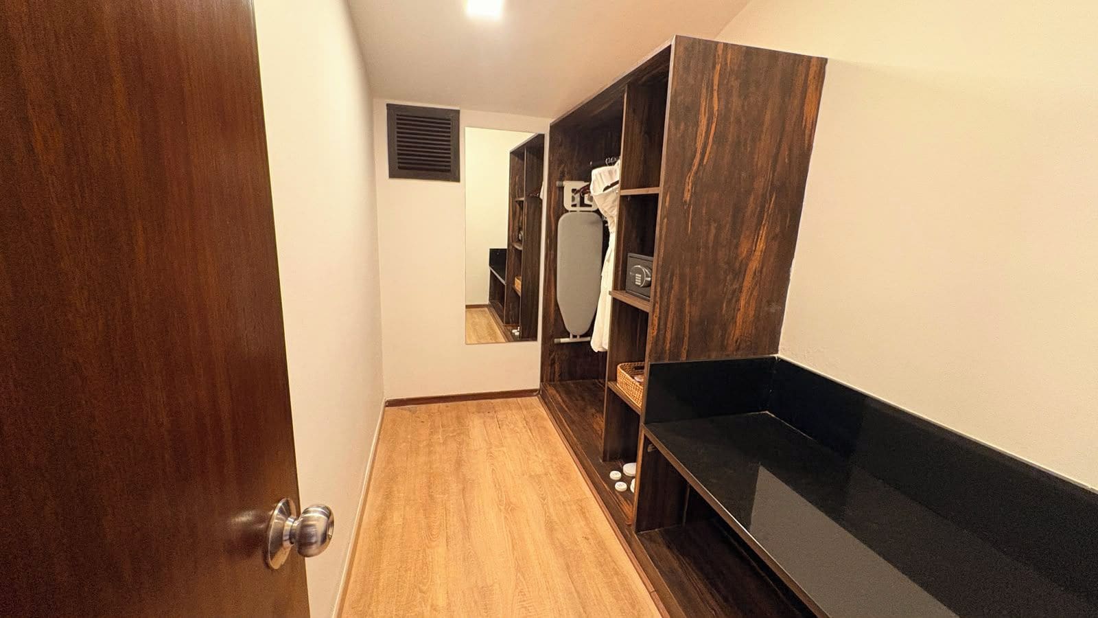A hotel room with a wooden floor, a black countertop, and a wardrobe with a mirror.