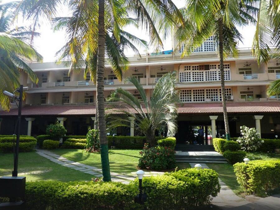 A multi-story hotel with a central courtyard, palm trees, and well-maintained gardens.