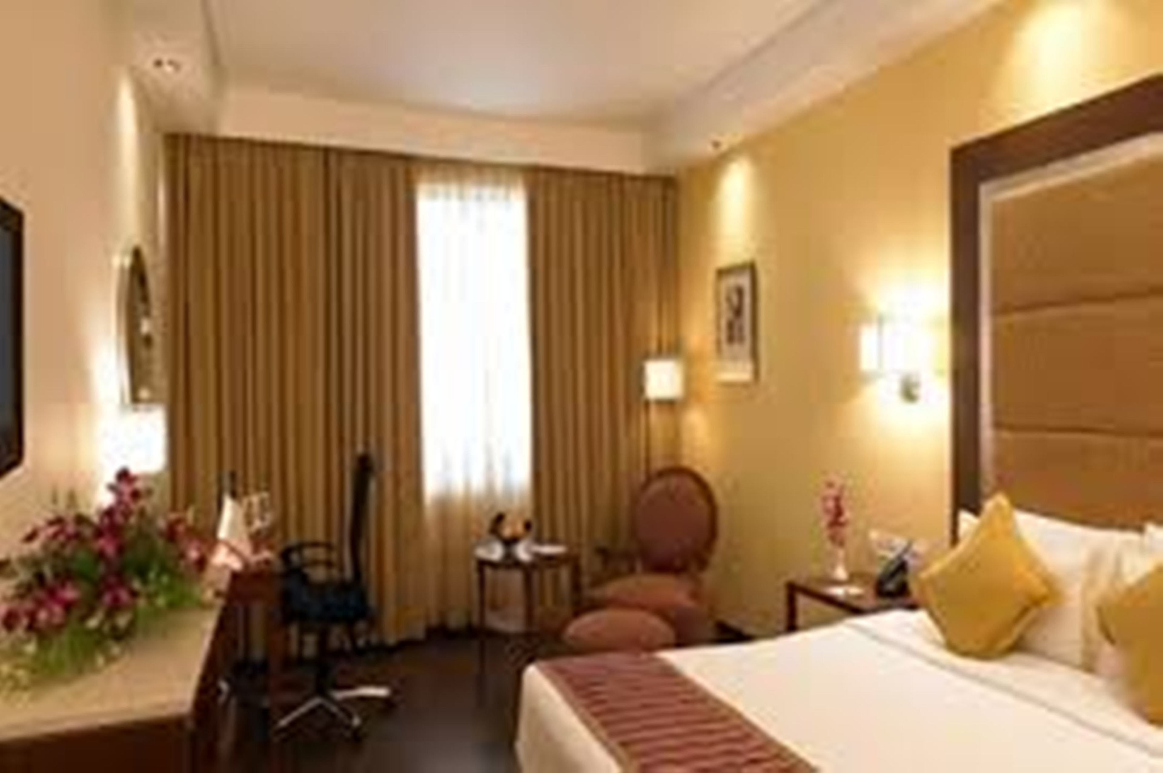 A hotel room with a bed, a desk, a chair, a small table, and a window with curtains.