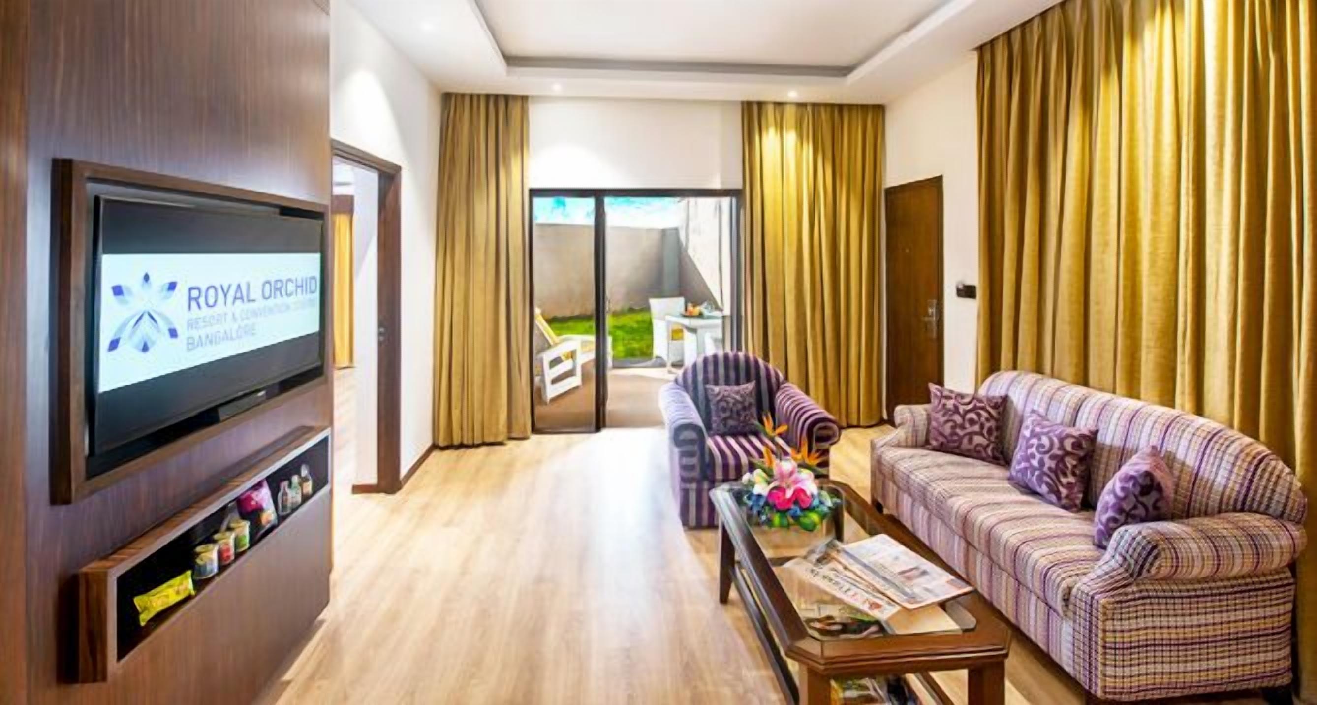A hotel room with a television, a sofa, a coffee table, and a view of the outdoors.