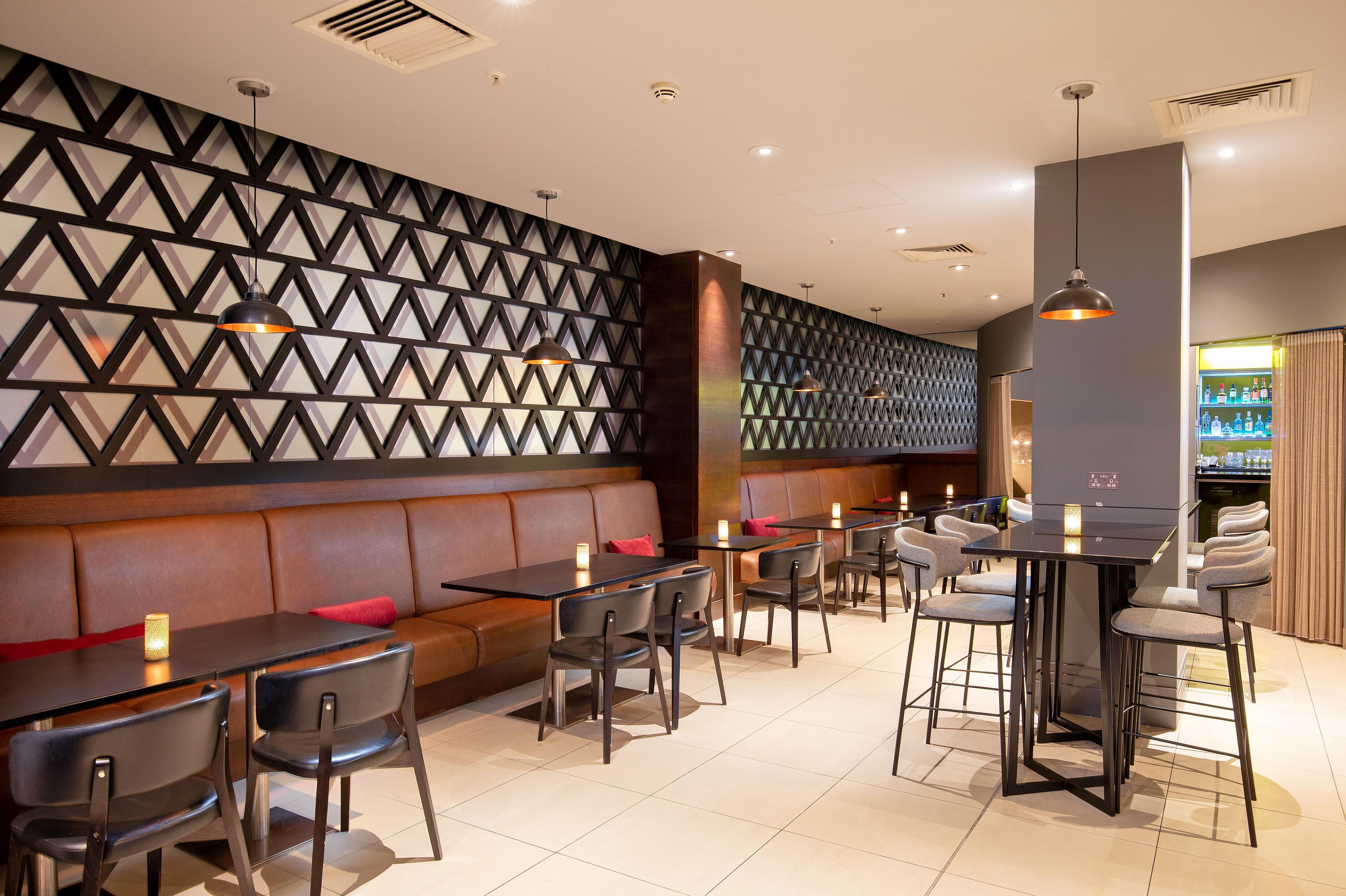 Un intérieur de restaurant moderne avec un mur aux motifs géométriques, des sièges en cuir et des luminaires suspendus.