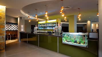 A bar area with a green counter, multiple hanging light fixtures, a fish tank, and a bar stocked with bottles.