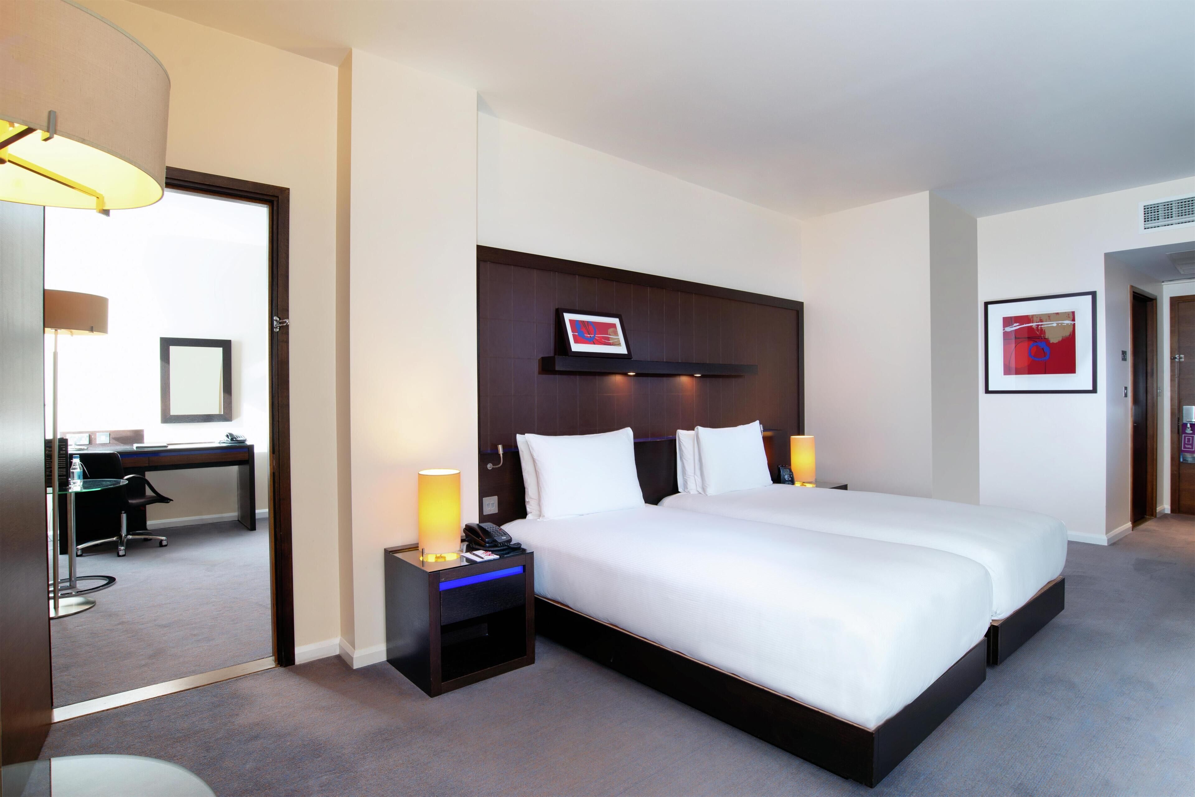 A hotel room with a large bed, bedside lamps, a desk, and a chair.