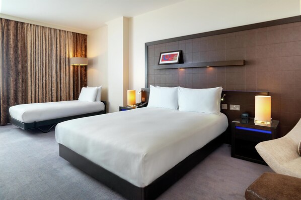 A hotel room with two beds, a headboard with a picture, bedside lamps, and a nightstand with a clock. - Hilton London Canary Wharf (London)