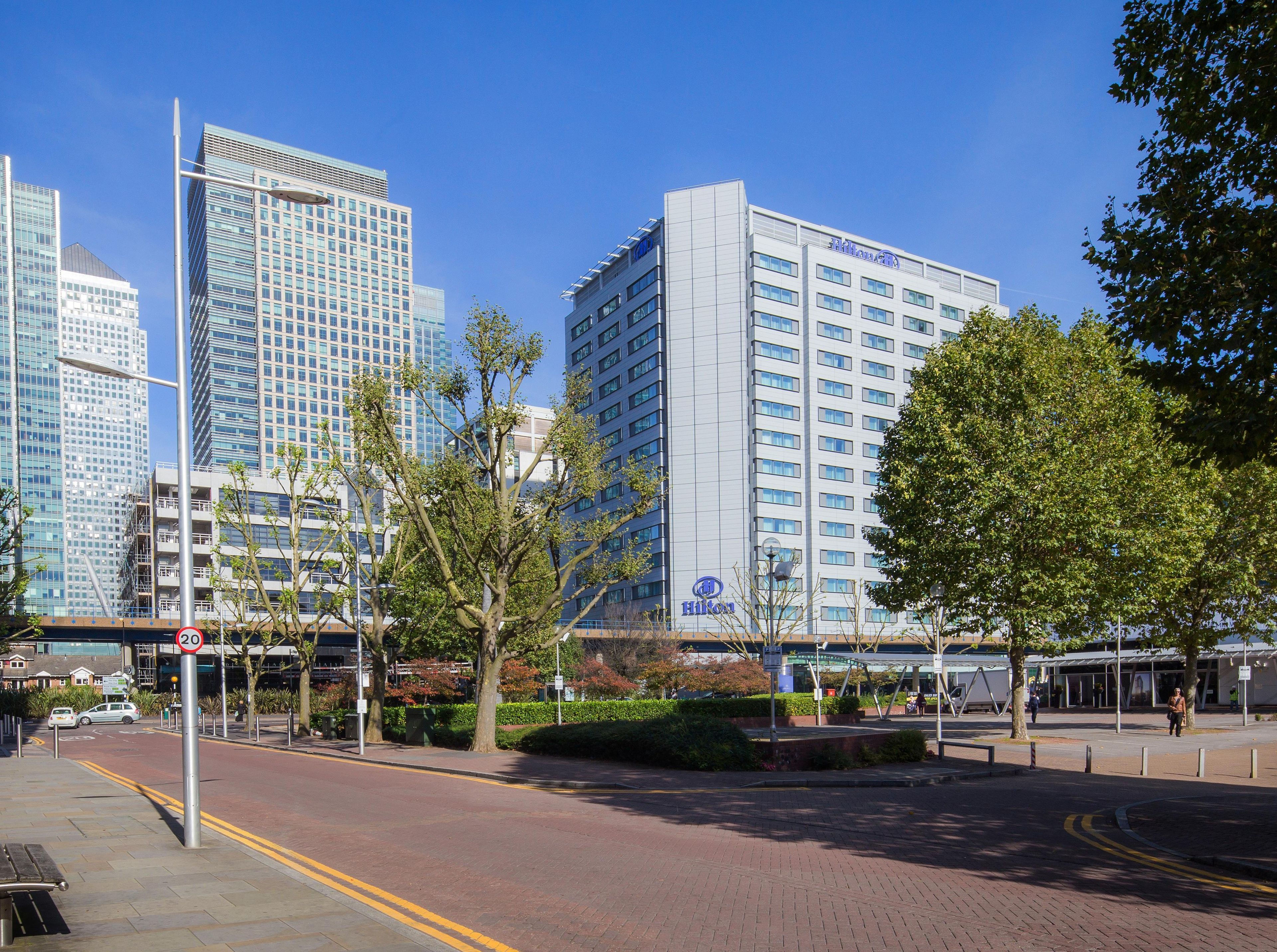 A modern hotel building with a clear sky, surrounded by trees and other high-rise buildings.