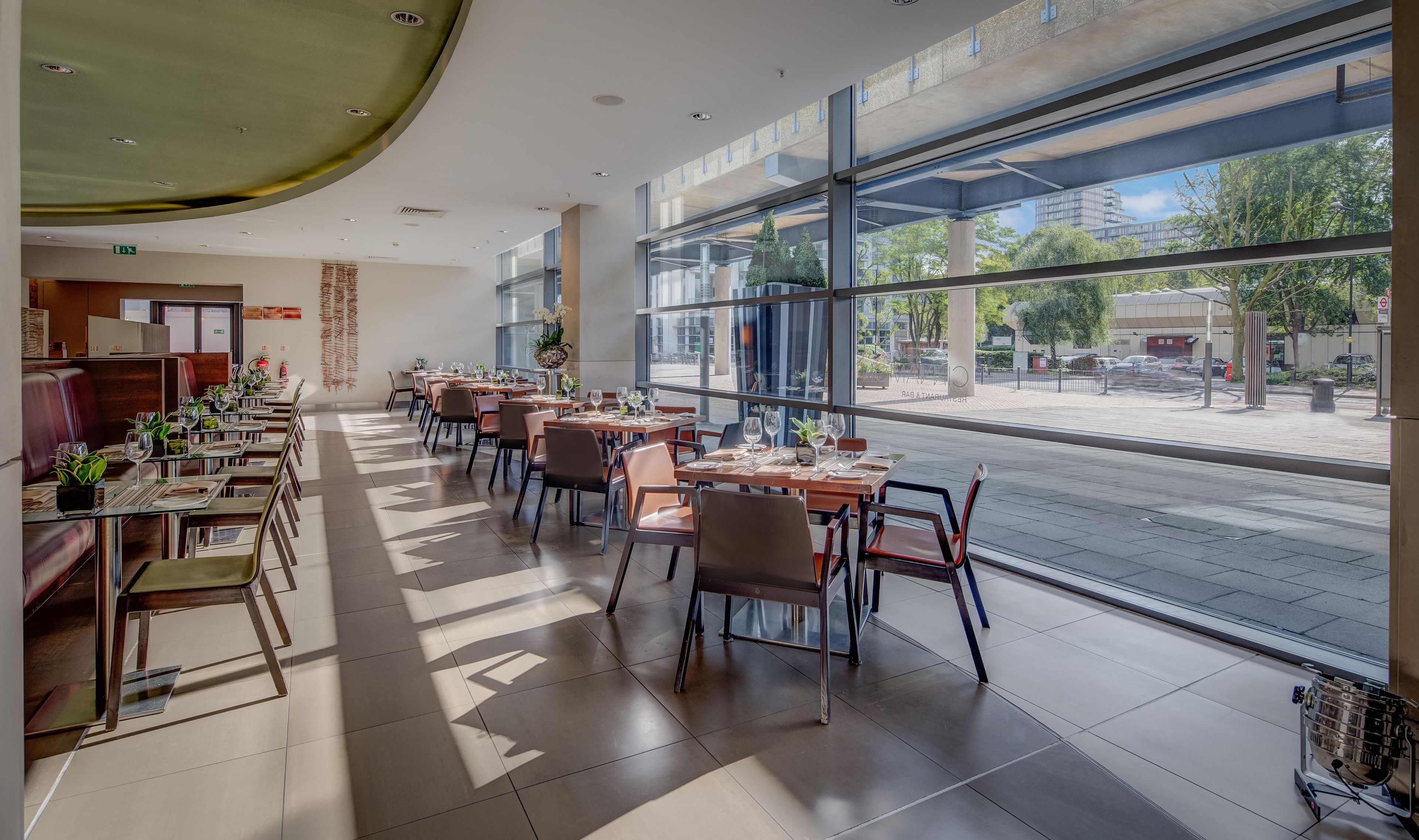 A modern restaurant with a long dining area, large windows, and a view of the street.