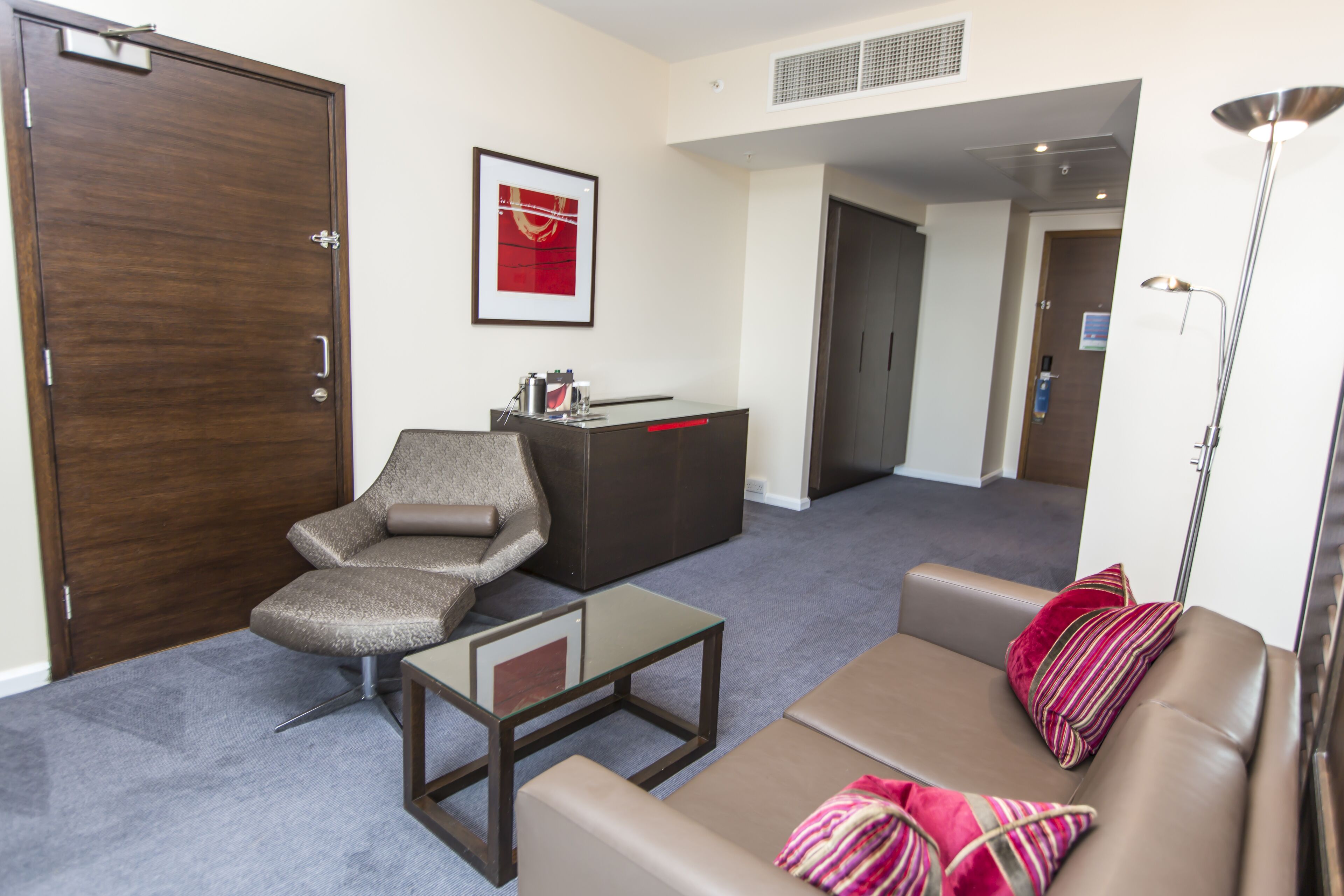 A modern hotel lobby with a brown leather sofa, a gray armchair, a glass coffee table, and a dark wooden reception desk.