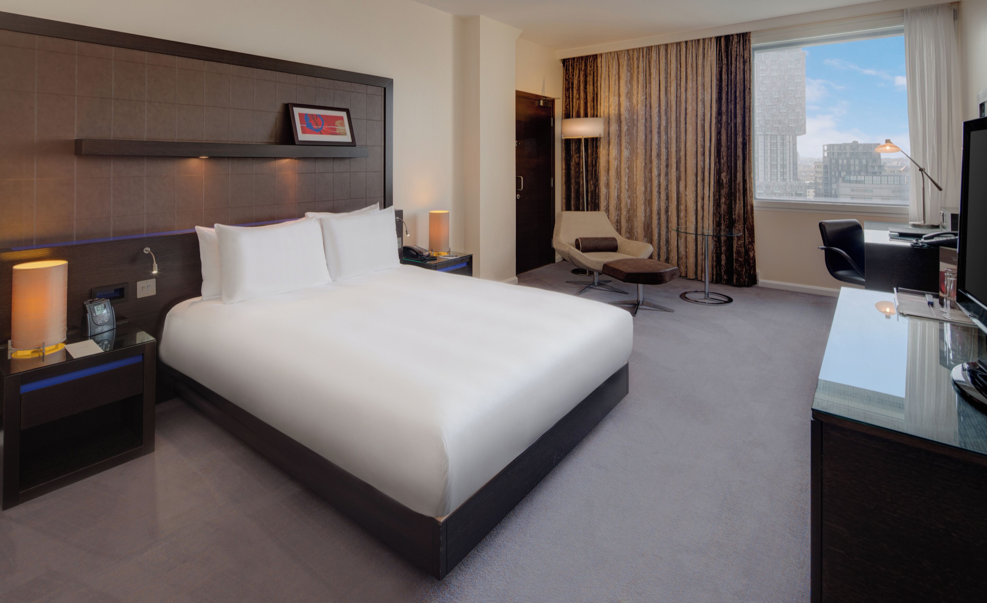 Ein Hotelzimmer mit einem großen Bett, einem Schreibtisch mit Stuhl, einem Fernseher und einem Fenster mit Vorhängen.