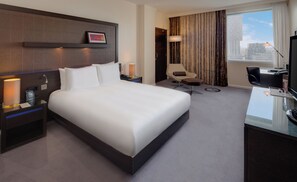 A hotel room with a large bed, a desk with a chair, a TV, and a window with curtains. - Hilton London Canary Wharf (London)