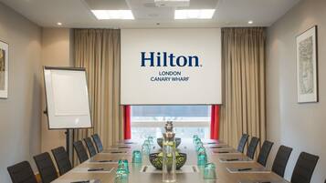 A conference room with a long table, chairs, a projector screen, and a large window with curtains.