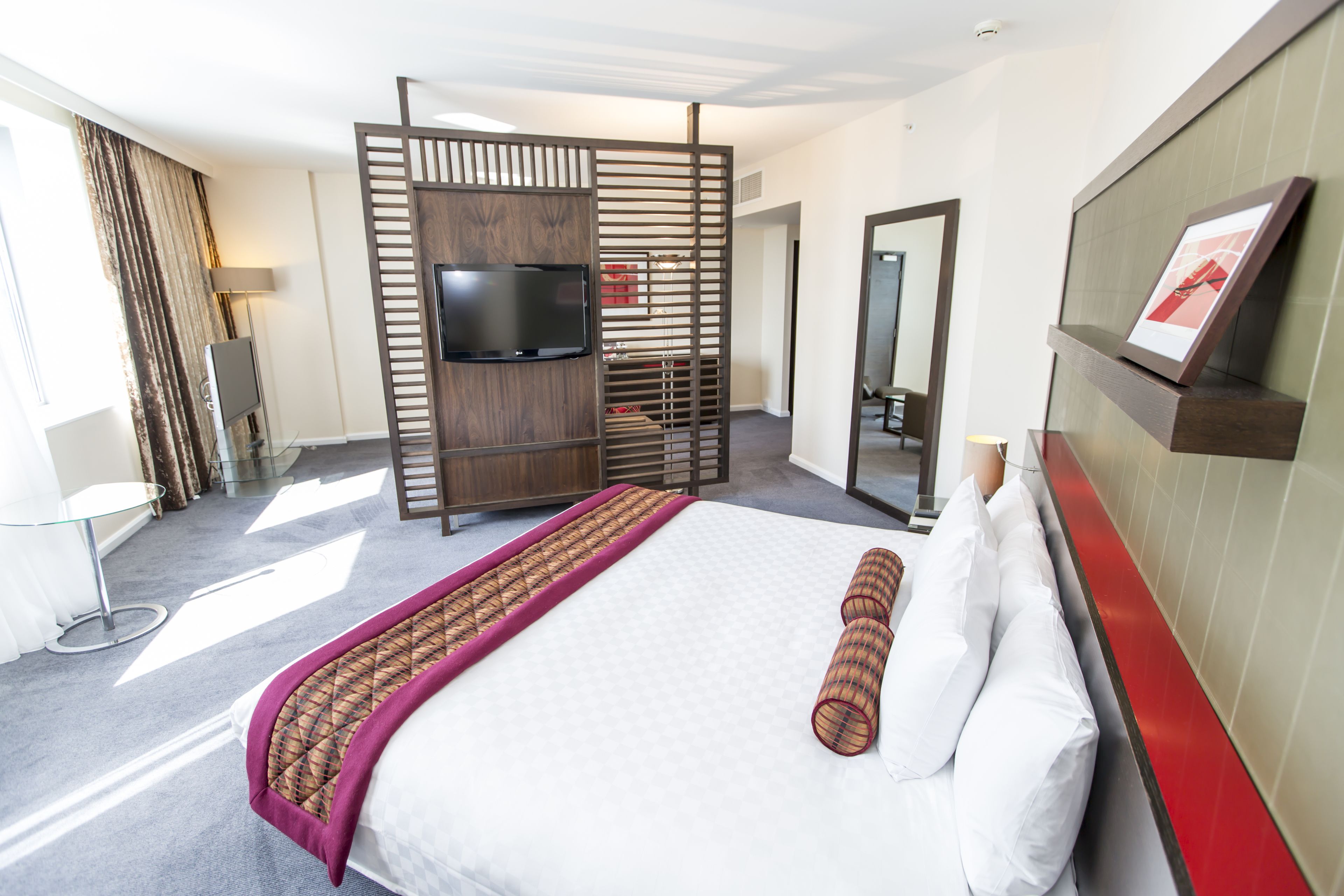 Ein Hotelzimmer mit Bett, Fernseher, Schreibtisch und Spiegel.