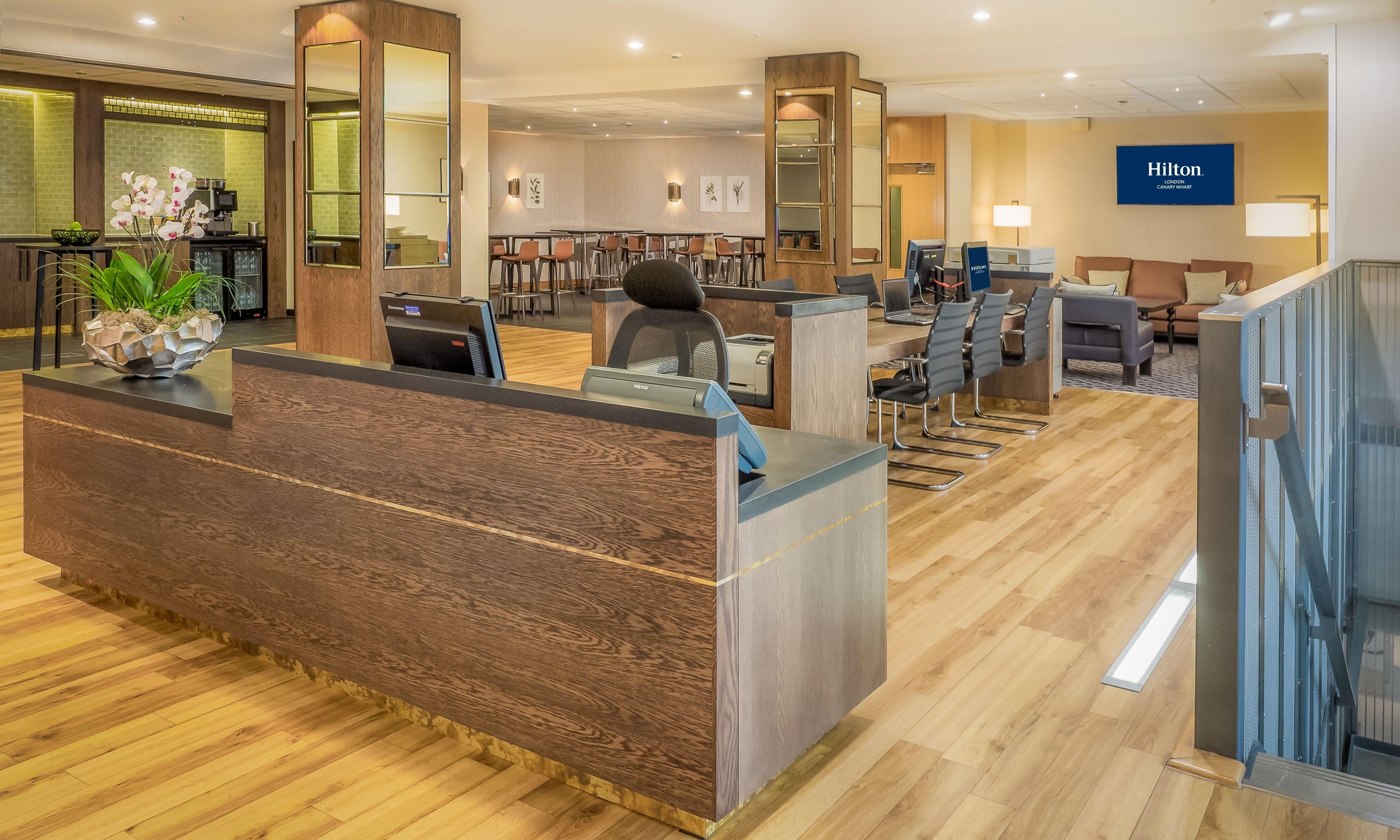 A hotel reception area with a wooden reception desk, seating area, and a Hilton sign.