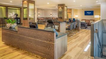 A hotel reception area with a wooden reception desk, seating area, and a Hilton sign.