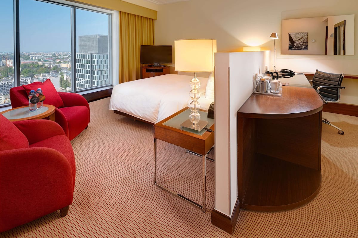 A hotel room with a bed, a desk, a chair, a TV, and a large window with a city view.