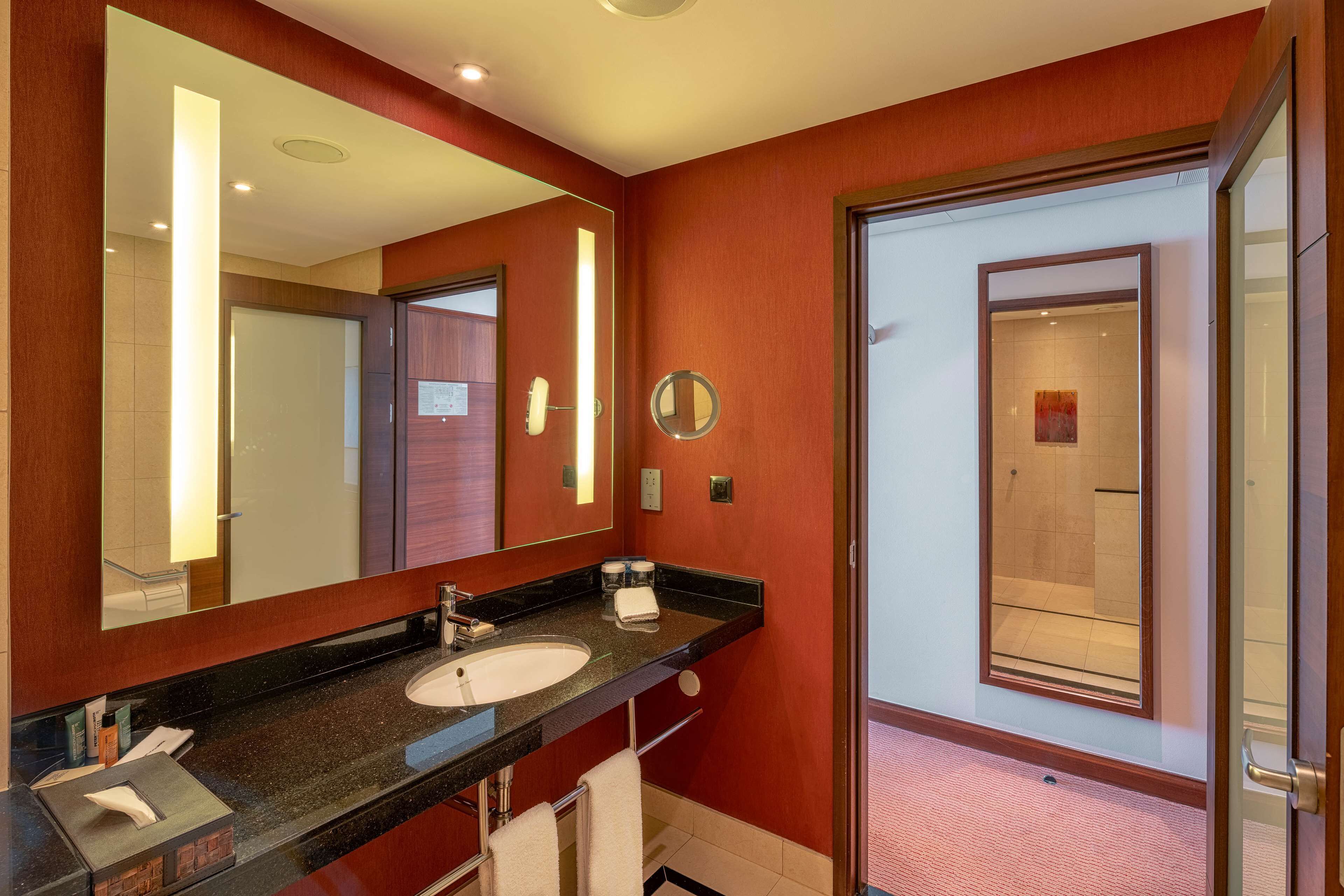 A hotel bathroom with a large mirror, a sink, and a shower area.