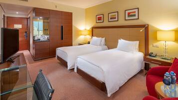 Een hotelkamer met twee bedden, een bureau met een stoel, een televisie en een rode fauteuil.