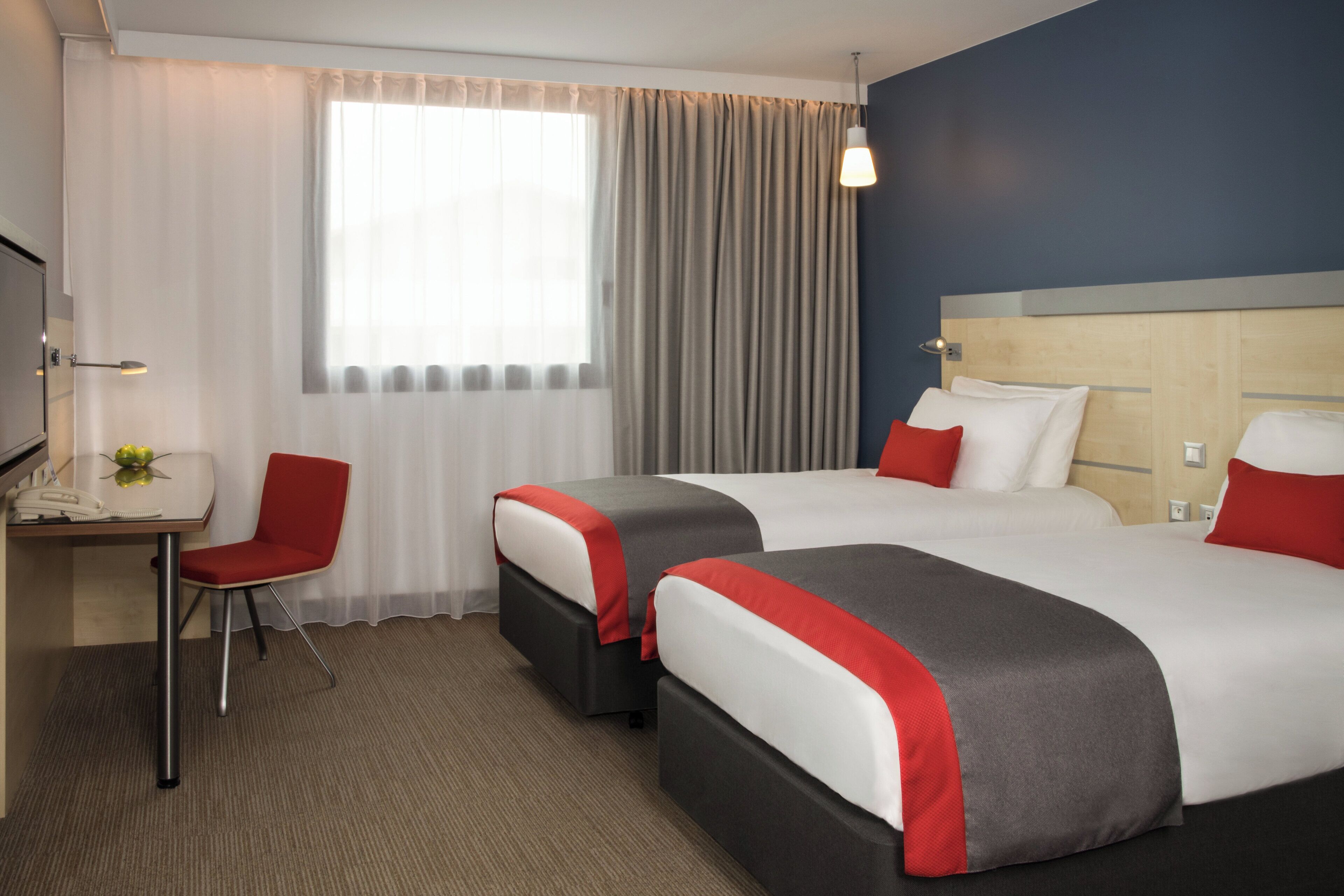 A hotel room with two beds, a desk, a chair, and a window with curtains.