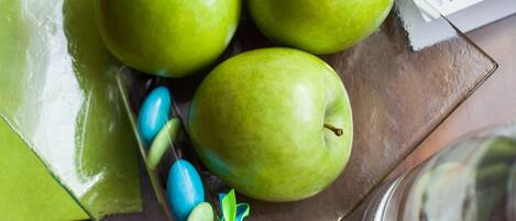 Un plato de vidrio con tres manzanas verdes y un lazo azul y verde, un vaso transparente y una computadora portátil sobre una mesa de madera.