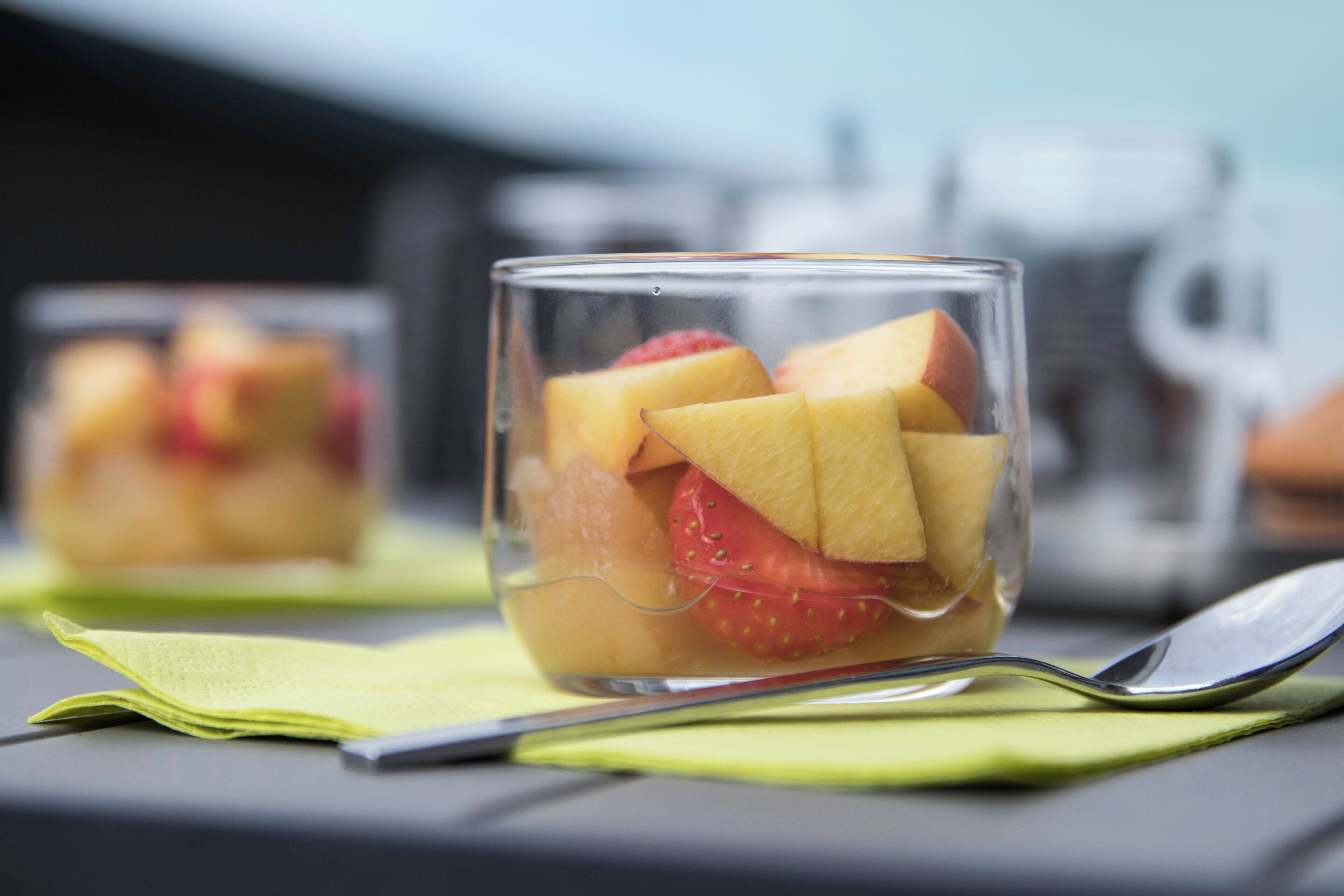 Een glazen glas met fruit, een lepel en een servet op een tafel.