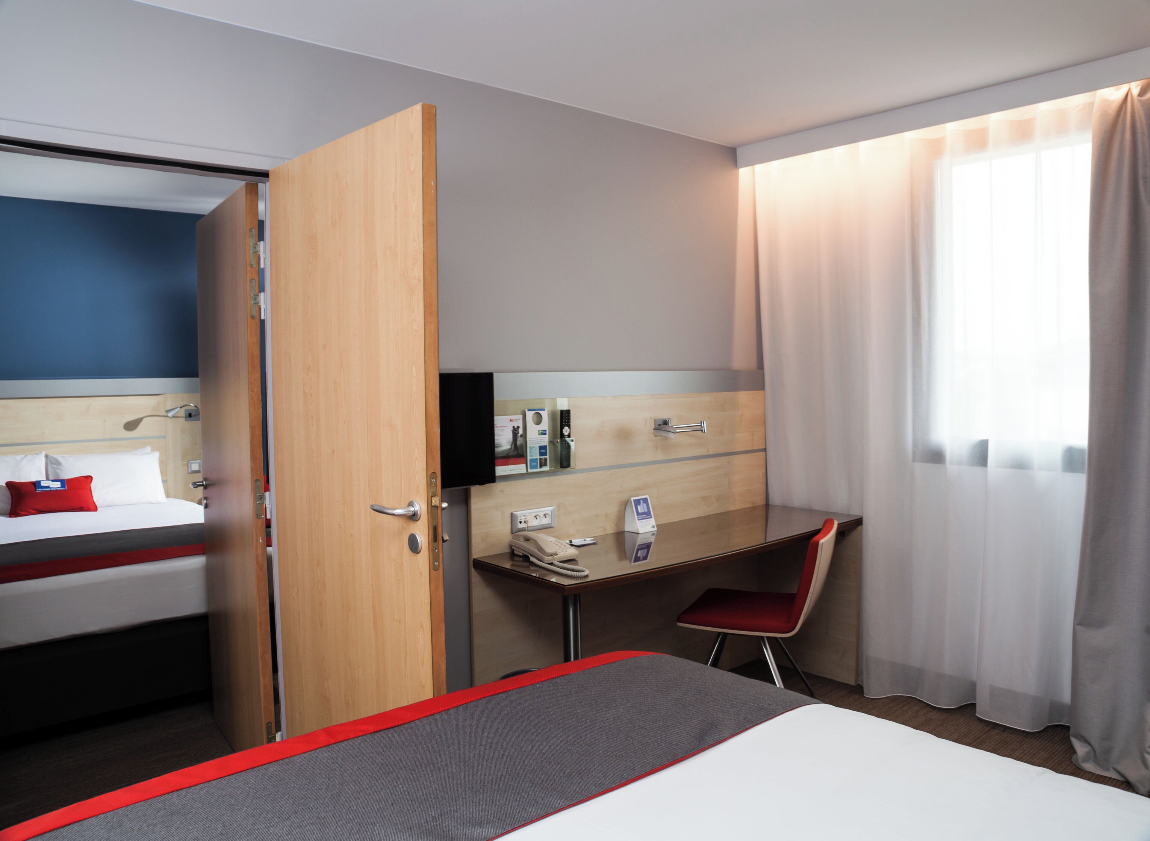 A hotel room with a bed, a desk, a chair, a TV, and a window with curtains.
