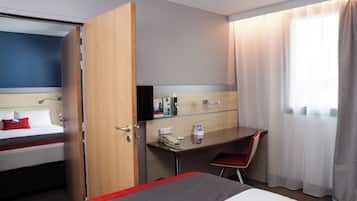 A hotel room with a bed, a desk, a chair, a TV, and a window with curtains.