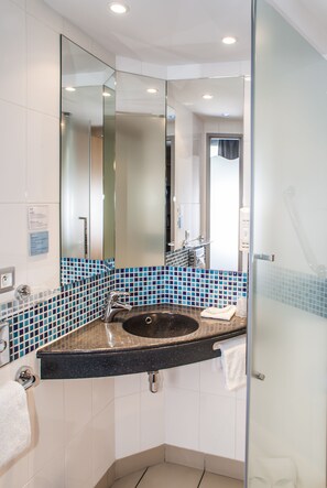 Une salle de bain moderne avec une douche à l’italienne en verre, un lavabo sur plan de toilette noir et des murs recouverts de carreaux bleus.