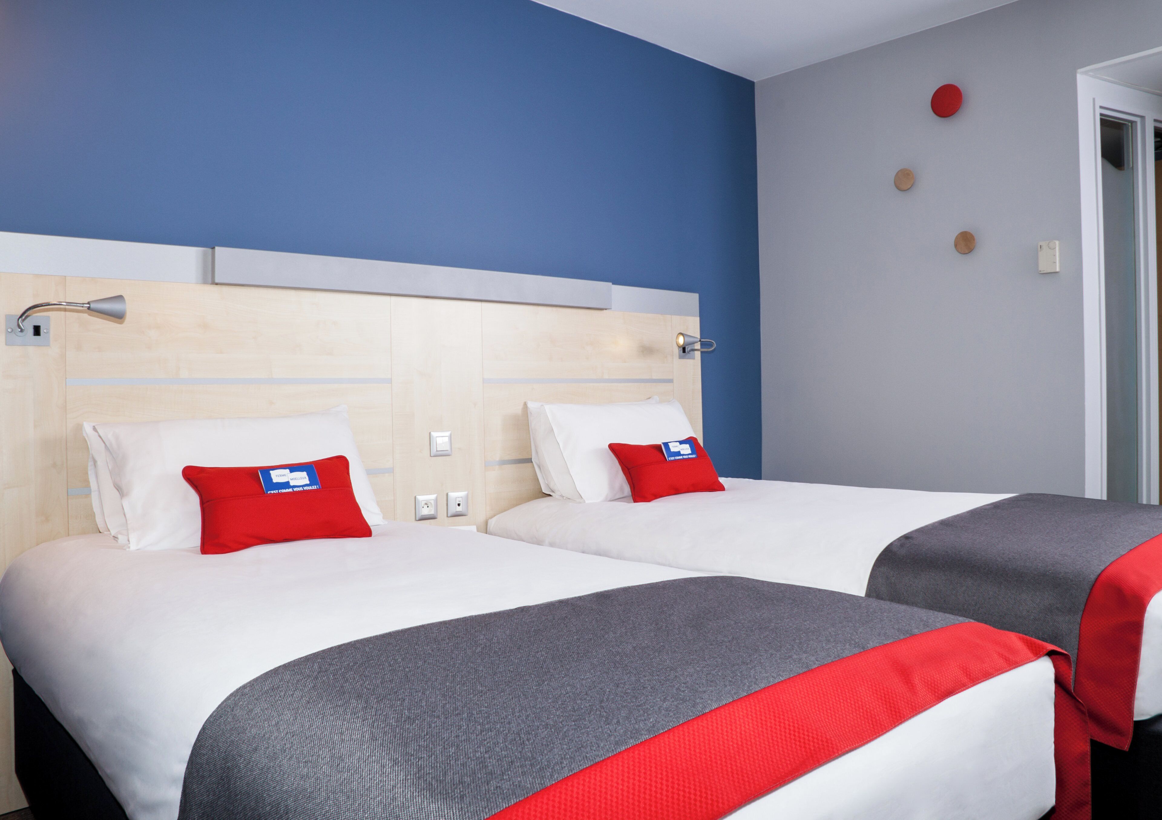Una habitación de hotel con dos camas, cada una con una almohada roja y una manta gris.
