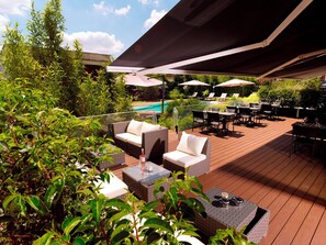 Une terrasse extérieure aménagée avec des meubles en osier, des parasols et une piscine en arrière-plan.