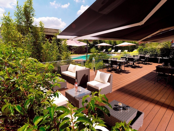 Un patio al aire libre con mobiliario de mimbre, sombrillas y una piscina al fondo.