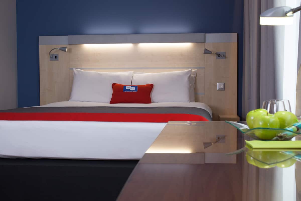 Ein Hotelzimmer mit Bett, Nachttisch, Lampe und Obstschale.