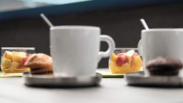 A table with a white cup, a glass with fruit, and a muffin.