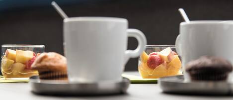 Una mesa con una taza blanca, un vaso con fruta y un muffin.