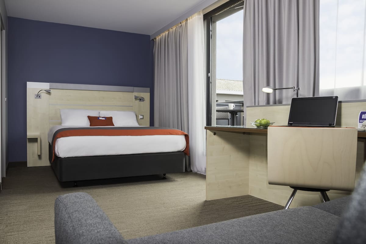 Ein Hotelzimmer mit Bett, Schreibtisch, Stuhl und einem Fenster mit Vorhängen.