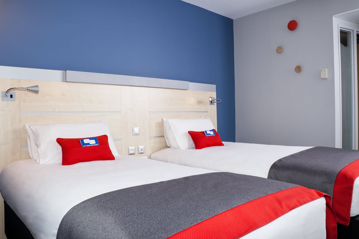 Ein Hotelzimmer mit zwei Betten, jeweils mit weißer Bettwäsche und roten Kissen, einem Holzkopfstück und einer blauen Wand.