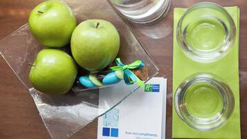 Een glazen schaal met groene appels, een koekje en een kaartje op een tafel.