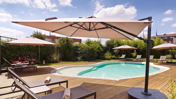 A poolside area with lounge chairs, umbrellas, and a wooden deck. - Holiday Inn Express Toulouse Airport by IHG (Blagnac)