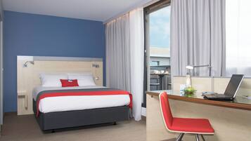 A hotel room with a bed, a desk with a laptop, a chair, and a window with curtains.