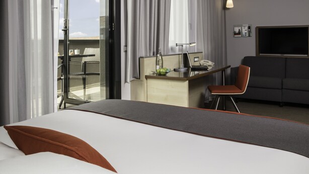 Une chambre d’hôtel avec un lit, un bureau avec un ordinateur portable, une chaise et un téléviseur.