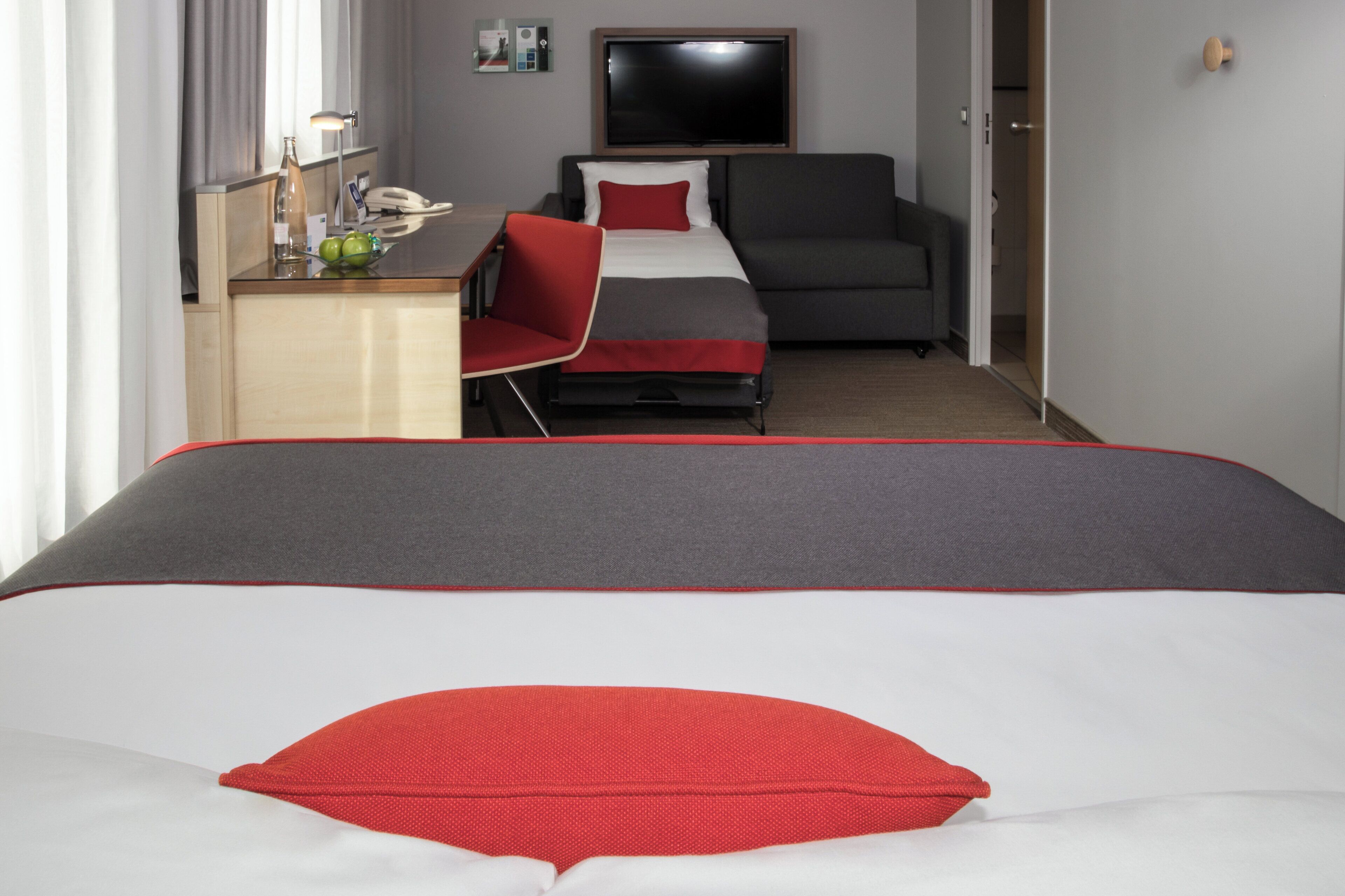 A hotel room with a bed, a desk, a chair, a television, and a door.