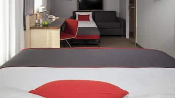 Una habitación de hotel con cama, escritorio, silla, televisor y puerta.