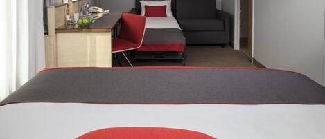 A hotel room with a bed, a desk, a chair, a television, and a door.